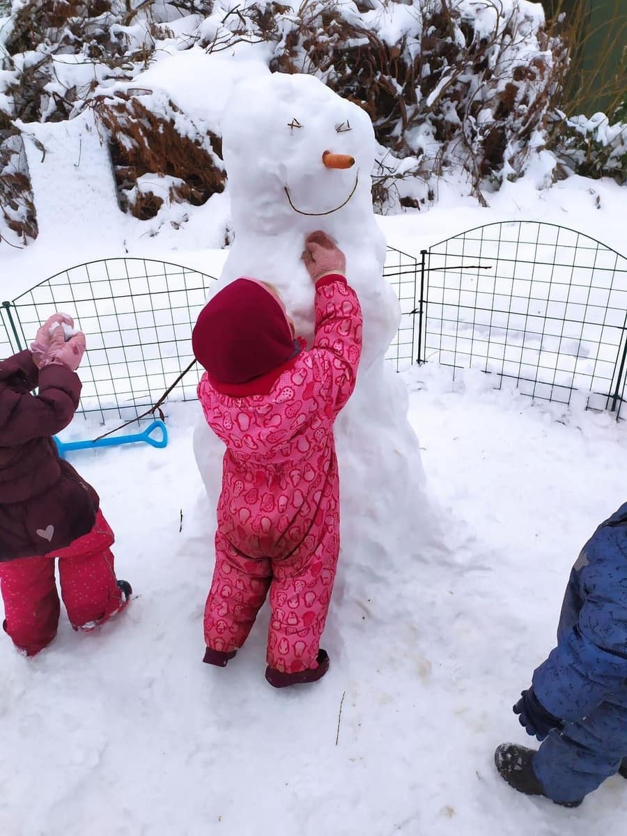 Kind von hinten baut einen Schneemann