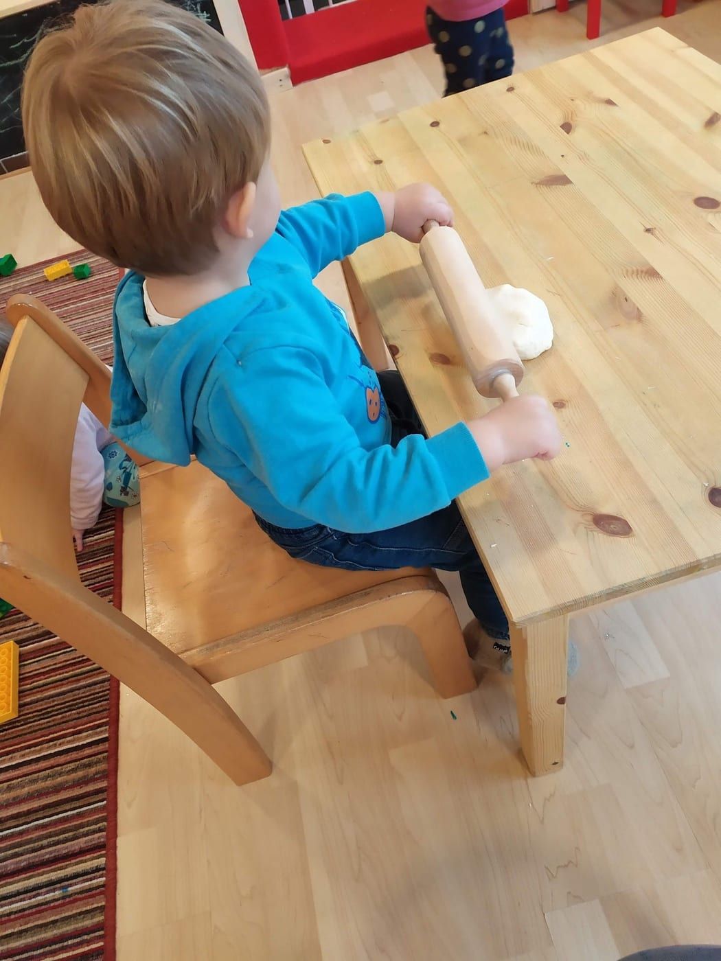 Kind von hinten knetet Teig am Holztisch